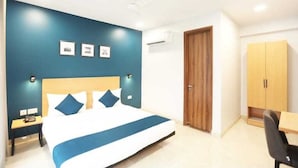 A hotel room with a large bed, a wooden wardrobe, a desk, and a nightstand. - Moody moon blue (Gurugram)
