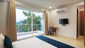 A hotel room with a large window, a bed, a desk, a chair, and a TV. - Moody moon blue (Gurugram)