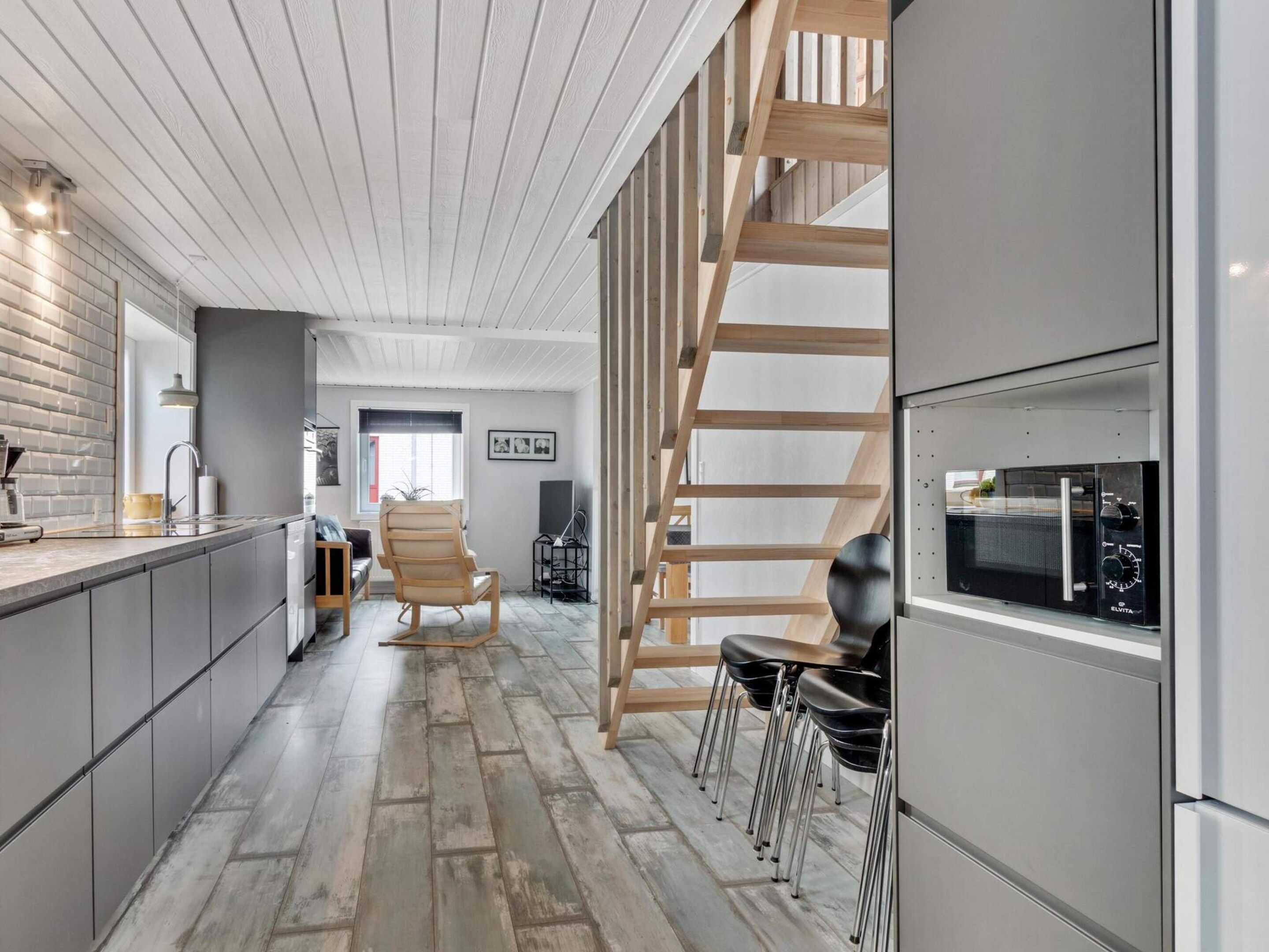 A modern kitchen with a built-in microwave, wooden staircase, and a seating area with chairs.