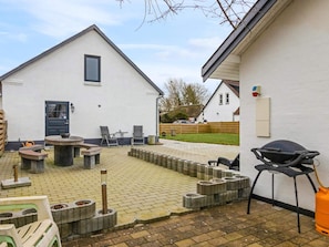 A patio area with a barbecue grill, outdoor seating, and a white building with a dark door. - 5 Star Holiday Home in Lokken (Lokken)