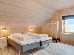 A bedroom with a sloped ceiling, wooden walls, a bed with pillows, a bedside table, and a window with a view. - 5 Star Holiday Home in Lokken (Lokken)