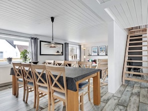 A dining area with a wooden table and chairs, a hanging pendant light, and a view of the outside through a window. - 5 Star Holiday Home in Lokken (Lokken)