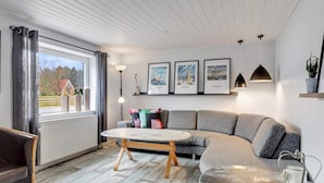 A modern living room with a sectional sofa, a round coffee table, and a view of a house through a large window. - 5 Star Holiday Home in Lokken (Lokken)