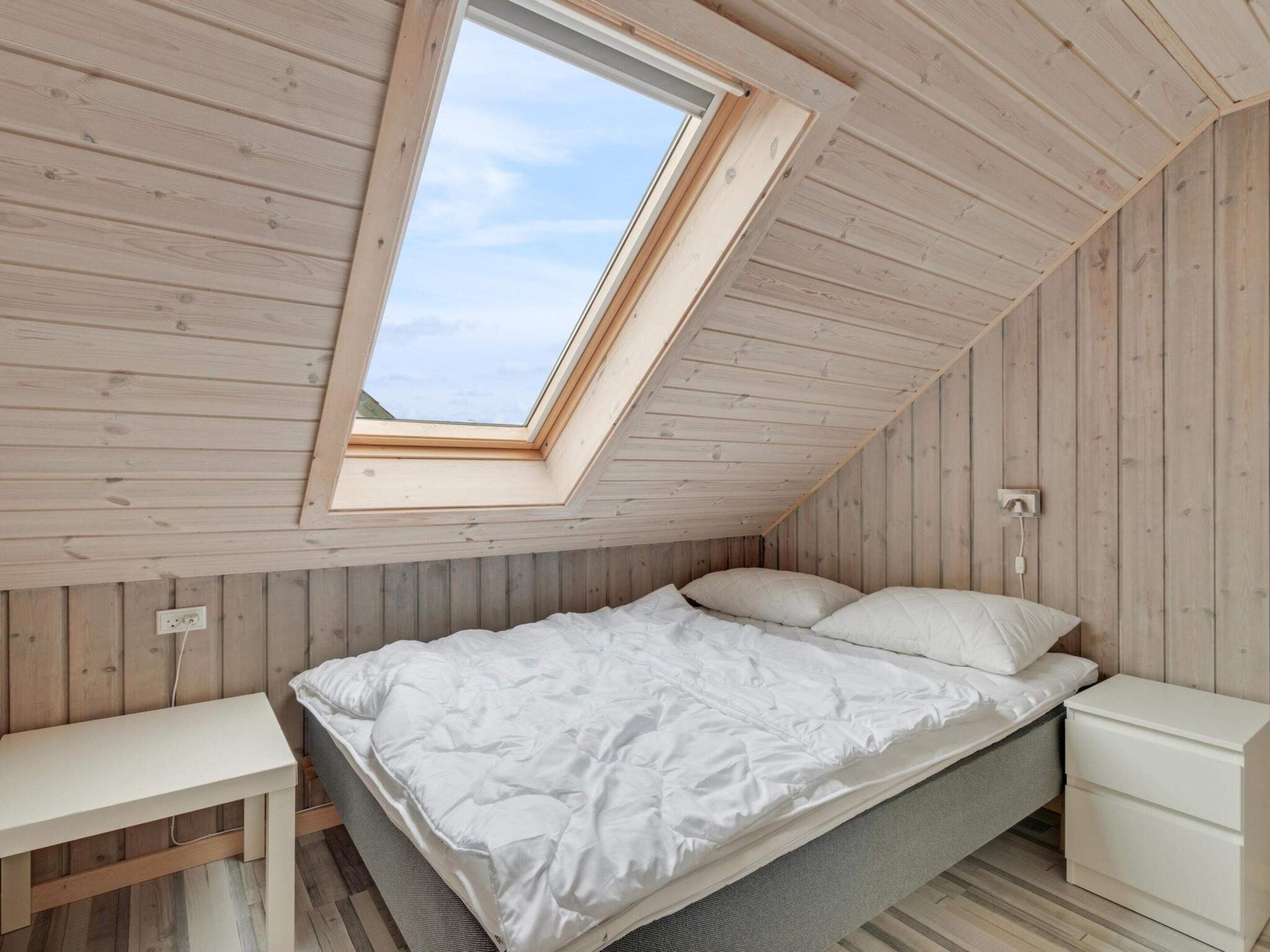Ein Schlafzimmer mit geneigter Decke, einem Oberlicht, einem Bett mit weißer Bettwäsche, einem Nachttisch und einem Beistelltisch.