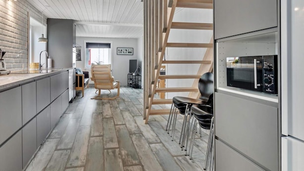 A modern kitchen with a built-in microwave, wooden staircase, and a seating area with chairs. - 5 Star Holiday Home in Lokken (Lokken)