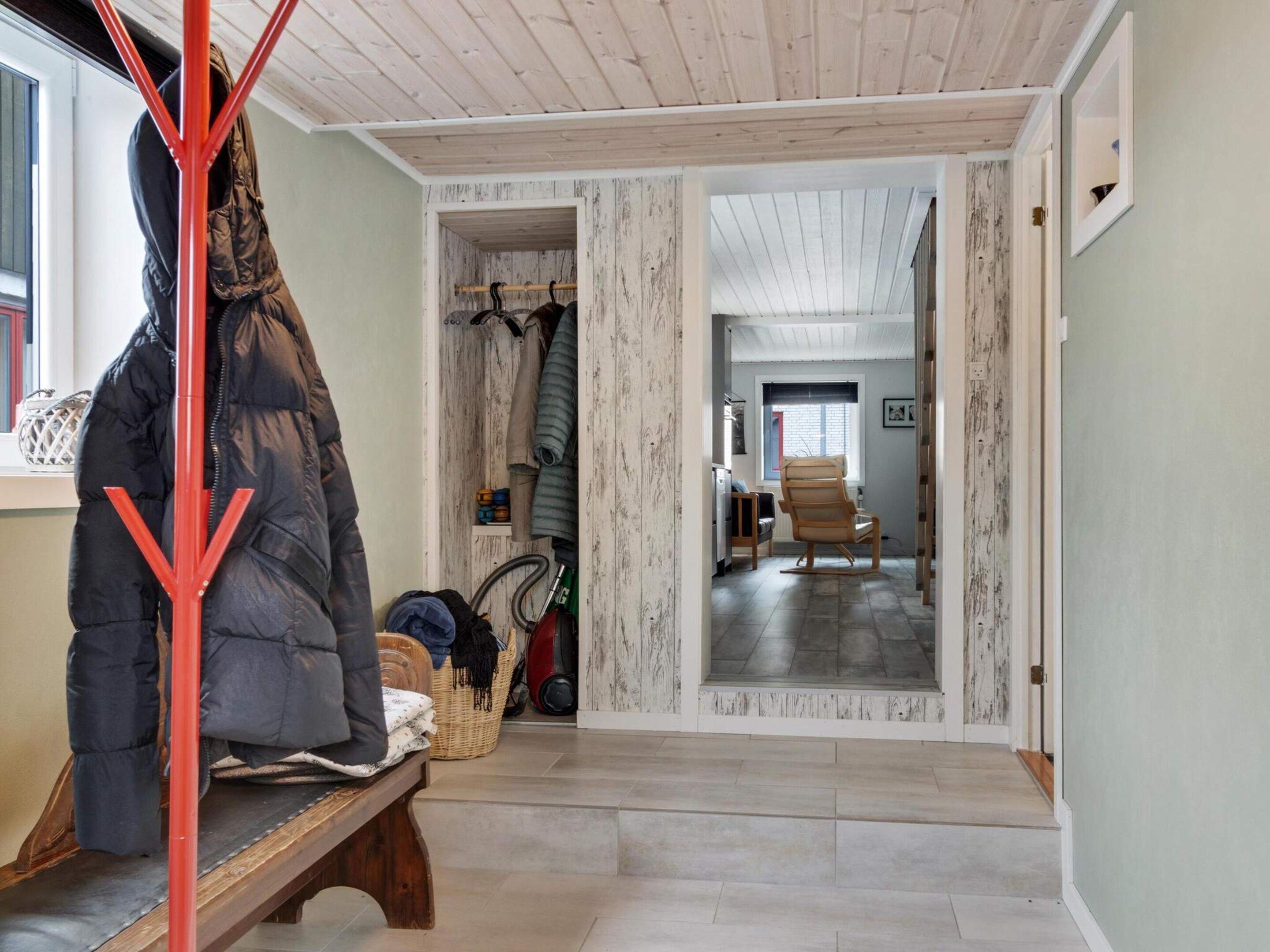 A hallway with a wooden bench, a coat rack, and a door leading to another room.