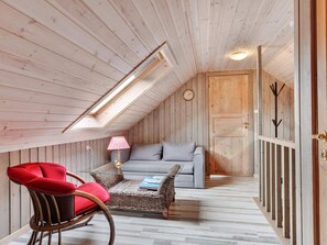 A cozy attic room with a sloped ceiling, a sofa, a red chair, a small table with a lamp, and a wooden door. - 5 Star Holiday Home in Lokken (Lokken)