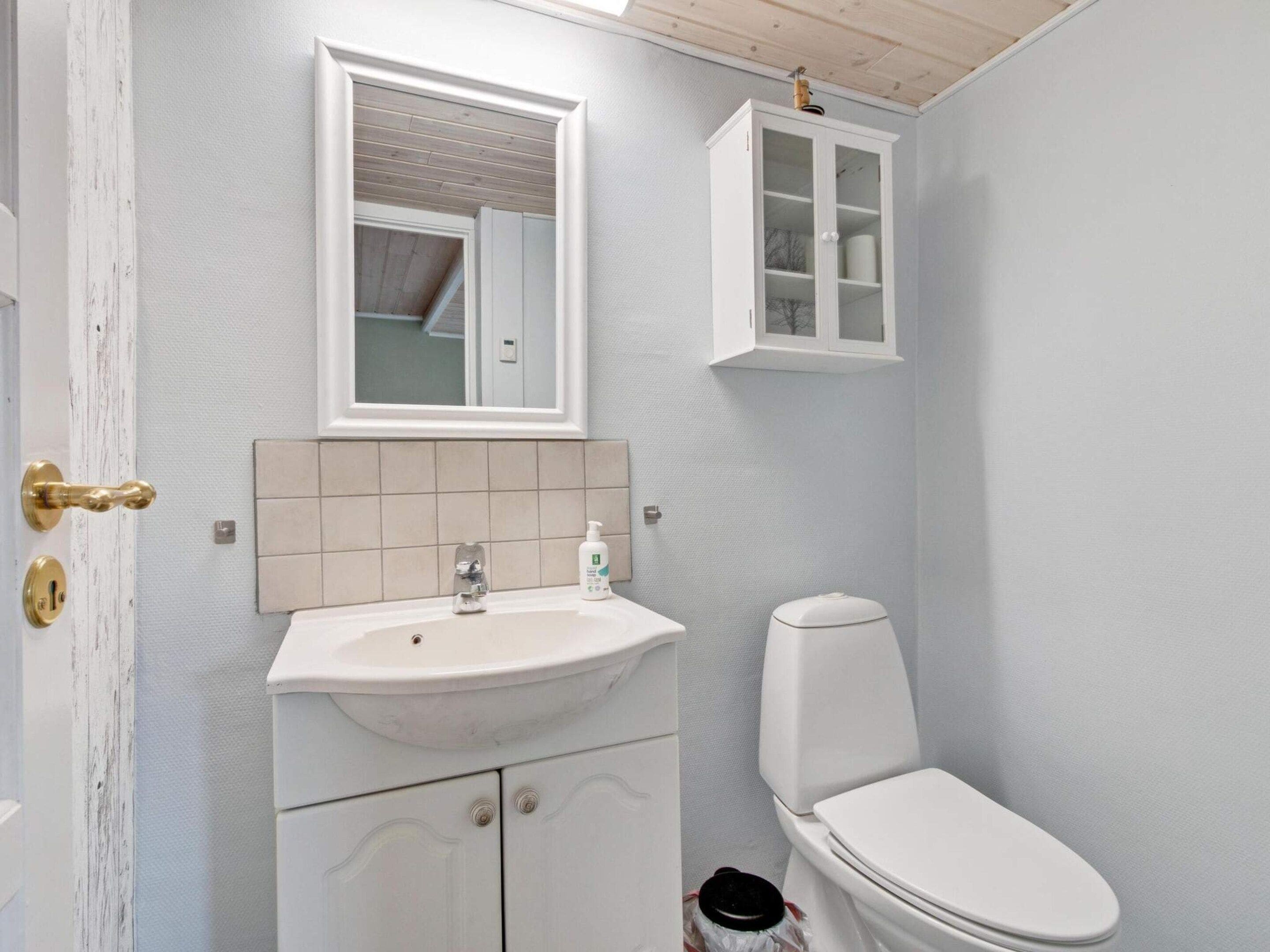A bathroom with a white sink, a mirror, a cabinet, and a toilet.
