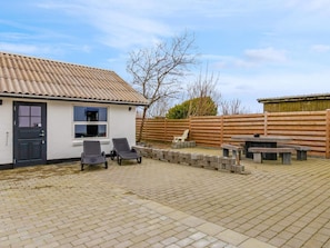 A house with a tiled roof, a black door, and a window. There are two lounge chairs and a table with benches in the yard. - 5 Star Holiday Home in Lokken (Lokken)