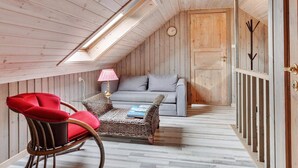 A cozy attic room with a sloped ceiling, a sofa, a red chair, a small table with a lamp, and a wooden door with a metal handle. - 5 Star Holiday Home in Lokken (Lokken)