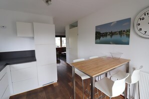 Een moderne keuken met witte kastjes, een houten eettafel en witte stoelen. Een grote klok hangt aan de muur.