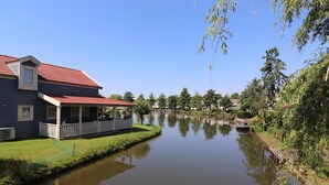 A house with a red roof and a porch, adjacent to a calm water body with reflections. - Bungalow in South Holland by the Water (Simonshaven)