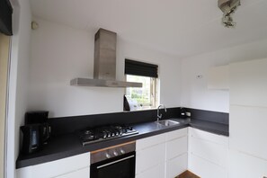 A compact kitchen with a gas stove, a coffee maker, and a window with a view. - Bungalow in South Holland by the Water (Simonshaven)