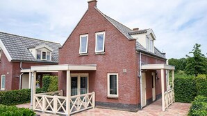 A two-story brick house with a covered porch and a small garden area. - Bungalow in South Holland by the Water (Simonshaven)