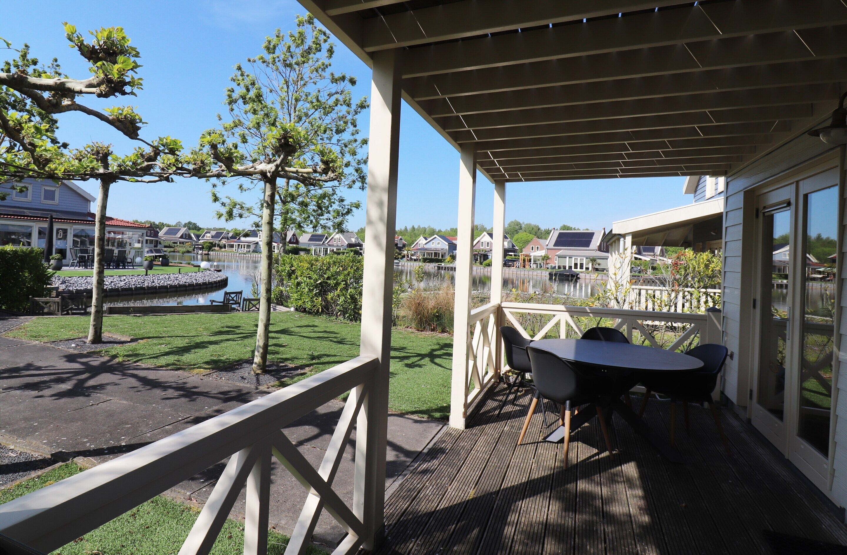 A covered outdoor area with a table and chairs, overlooking a body of water and residential buildings.