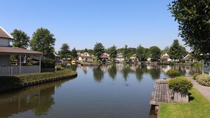 Un lago tranquilo con casas a la otra orilla, un muelle de madera y un pequeño puente.