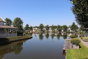 Een rustig meer met huizen aan de overkant, een houten steiger en een kleine brug.