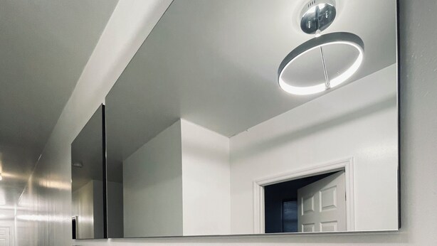 A modern hallway with a mirrored wall, a ceiling light, and a door leading to a bedroom.