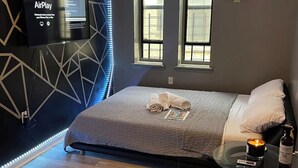 A modern bedroom with a bed, a TV, and a small table with a candle and a bottle.