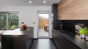 Una cocina moderna con armarios oscuros, una pared de acento de madera y vistas a una terraza de madera a través de una puerta de vidrio.