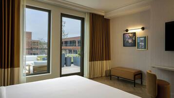A hotel room with a large bed, a bench, a TV, and a balcony with outdoor furniture.