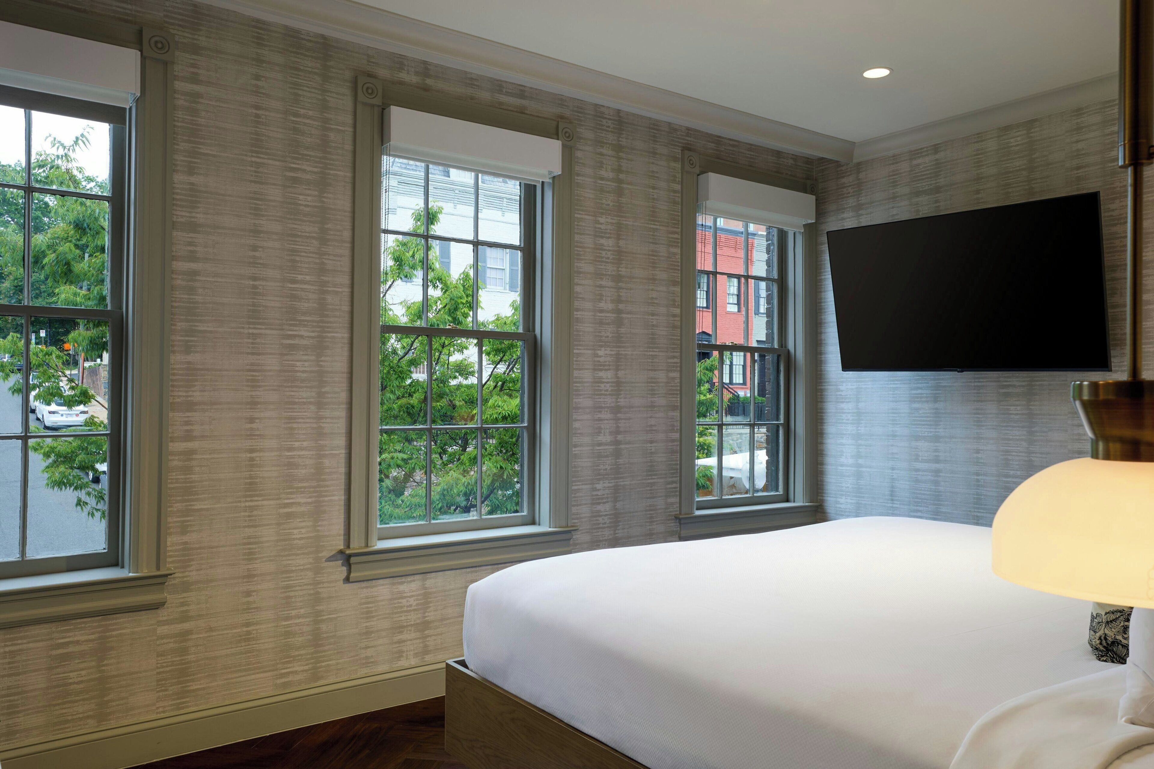 A hotel room with a large bed, a flat-screen TV mounted on the wall, and large windows offering a view of the outside.