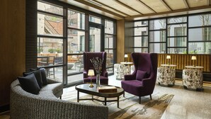 Eine geräumige Lobby mit großen Fenstern, einer Sitzecke mit Sofa und Sesseln sowie einem Couchtisch mit Vase und Buch.