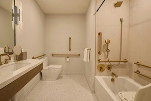 A bathroom with a white sink, toilet, and bathtub, equipped with gold fixtures and grab bars.