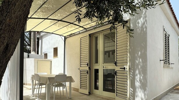 A covered patio area with a table and chairs, a sliding glass door, and a tree providing shade. - Miramare House - Trilo 5 D (Puglia)