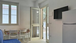 A compact kitchen with a dining area, a TV mounted on the wall, and a sliding glass door leading outside. - Miramare House - Trilo 5 D (Puglia)