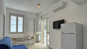 A compact kitchen with a white refrigerator, a dining table with chairs, and a blue sofa. - Miramare House - Trilo 5 D (Puglia)