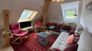 A loft-style room with a sloped ceiling, a built-in desk, a sofa, and a red patterned rug. - Bright apartment in Villard-de-Lans, 58 m², 2 bedrooms, near Vercors activities (Villard-de-Lans)