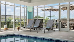 Un espace piscine équipé de chaises longues et de parasols, de grandes fenêtres et offrant une vue sur l’extérieur.