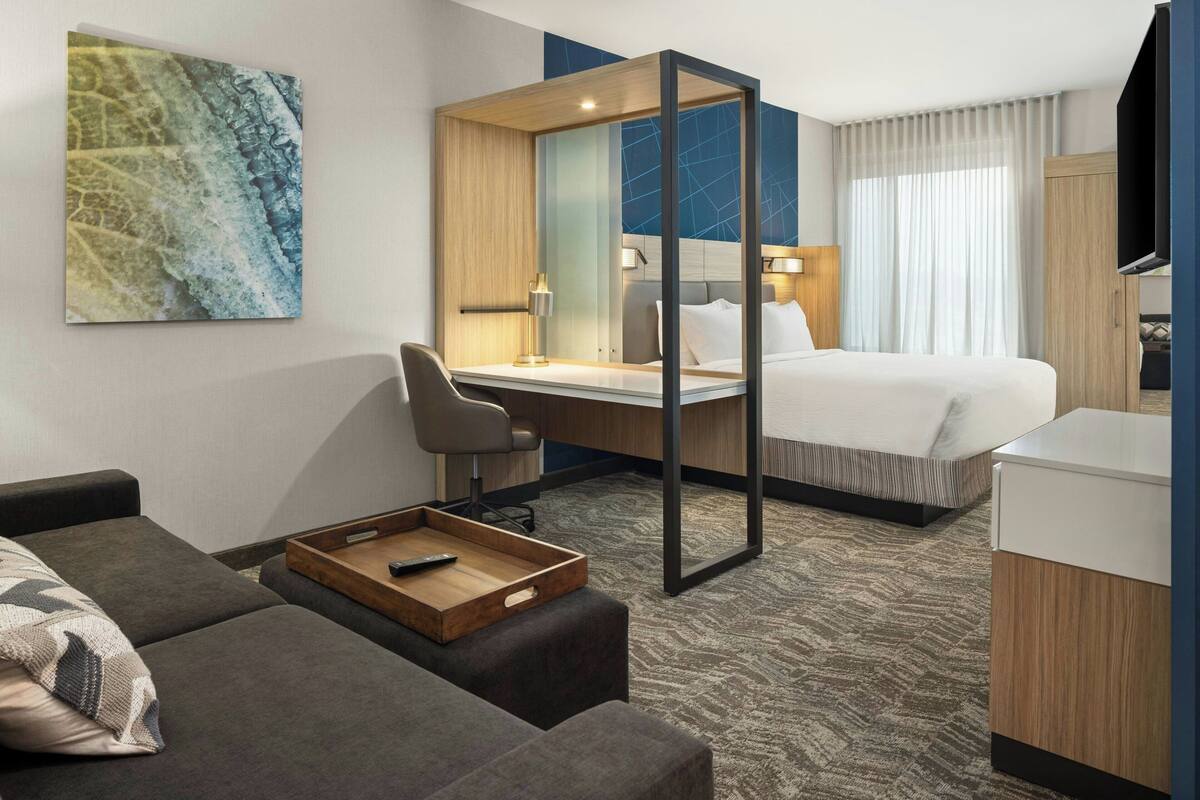 A modern hotel room with a bed, a desk, a sofa, and a TV.