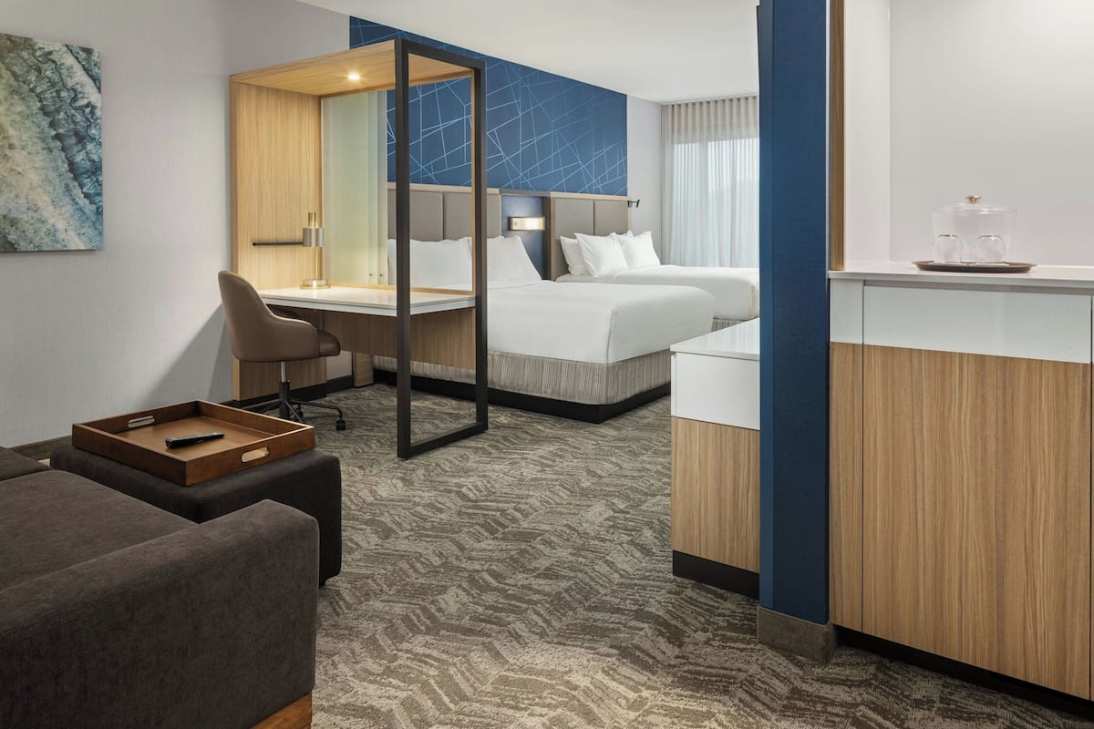 A hotel room with a bed, a desk, a chair, a small sofa, and a tray table.