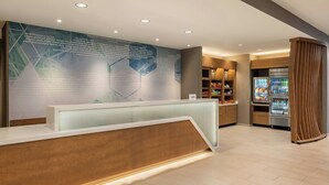 Un espace d’accueil au design moderne, comprenant un comptoir de réception, un grand panneau d’affichage et un réfrigérateur rempli de boissons.