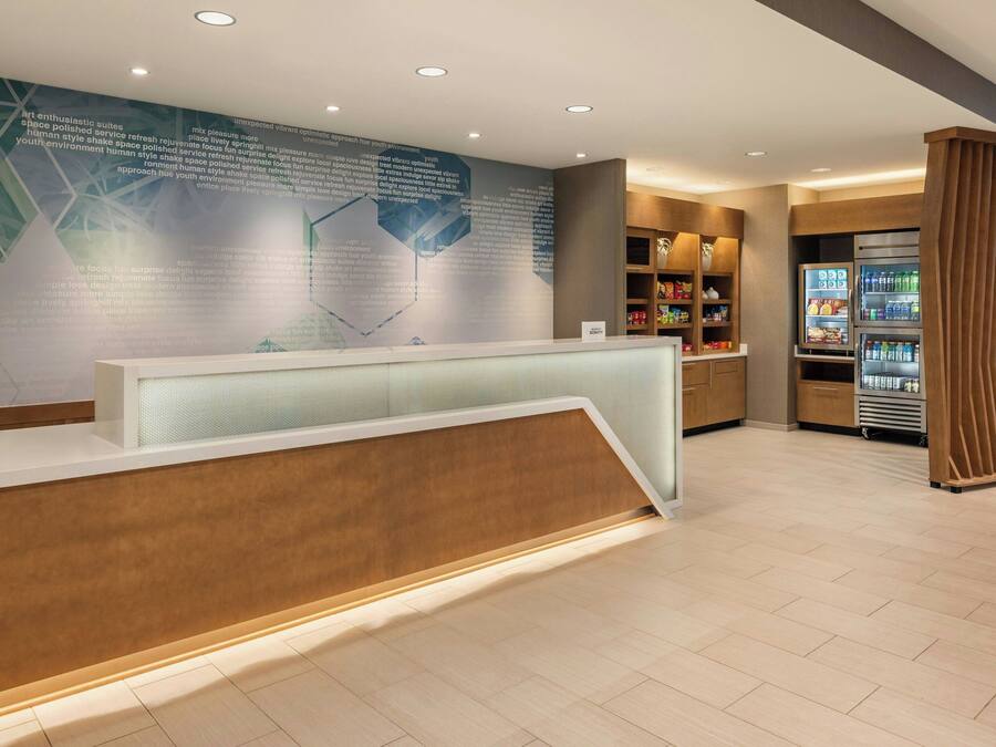 A reception area with a modern design, featuring a reception desk, a large informational wall, and a refrigerator stocked with beverages.