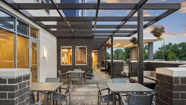 Une terrasse extérieure avec des tables et des chaises, un mur en briques et des jardinières suspendues.