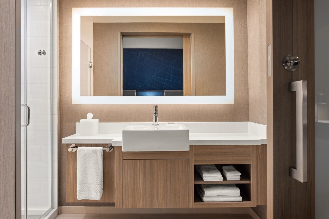 A modern bathroom with a large mirror, white sink, and wooden cabinets.