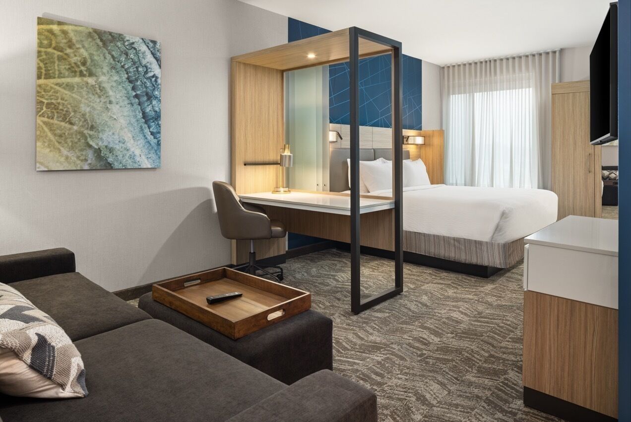 A hotel room with a bed, a desk, a chair, a sofa, and a TV.
