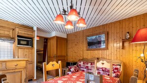 A cozy room with a wooden ceiling, a bed with a heart-shaped headboard, a dining table with a red heart-patterned tablecloth, and a kitchen area with wooden cabinets and a microwave.