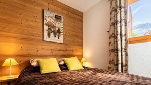 A bedroom with a wooden headboard, two bedside lamps, a bed with a brown patterned bedspread, and a window with curtains.
