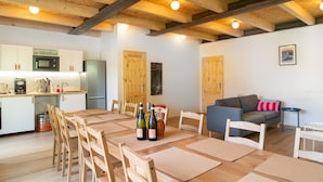 Uma cozinha com vigas de madeira, uma sala de jantar com mesa e cadeiras, e um sofá numa sala de estar.