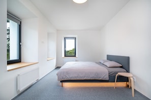 A modern bedroom with a large bed, a small stool, a window, and a radiator. - Villa in Desna Near Ski Resorts (Desna)