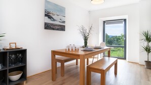 Uma área de refeições moderna com uma mesa de madeira, bancos e vista para o verde através de uma grande janela.