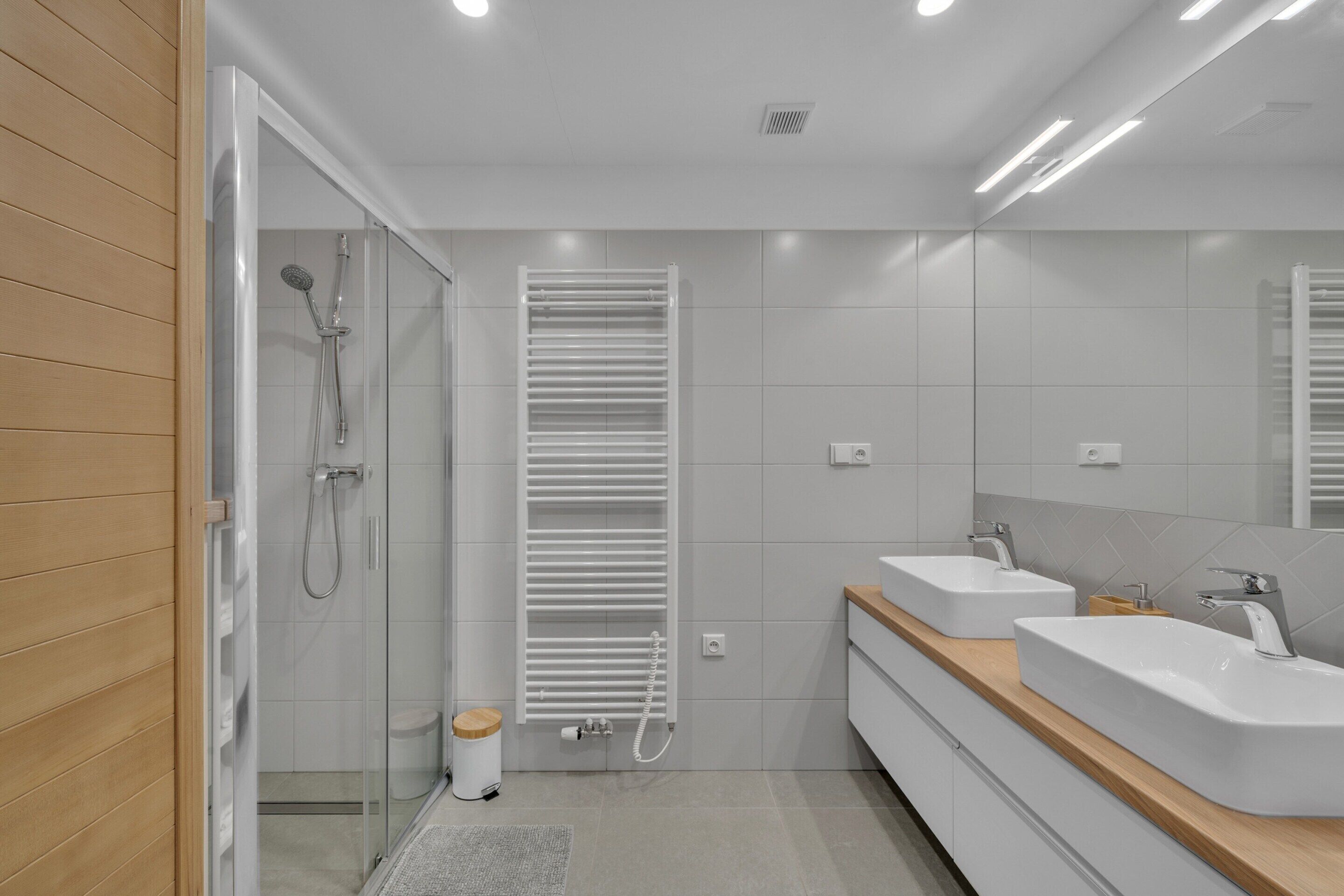 A modern bathroom with a glass shower enclosure, a built-in towel rack, and a vanity with two sinks.