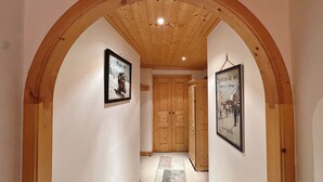A hallway with wooden ceiling and walls, framed pictures on the walls, and a wooden door at the end.