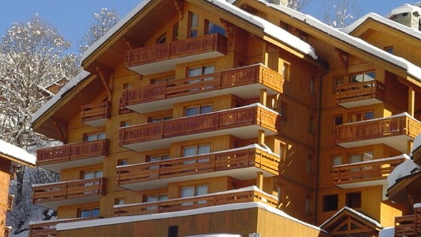 A multi-story wooden chalet with balconies, surrounded by snow.