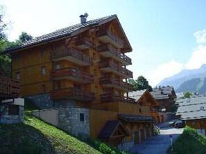 A multi-story wooden building with balconies, set against a mountainous backdrop.