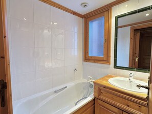 A bathroom with a white bathtub, wooden vanity, and a mirror above the sink.